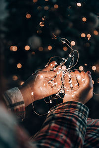 Close-up photo of female hands holding fairy lights in front of christmas tree