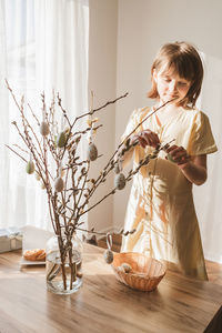 A cute little girl hangs decorative textile easter eggs on a willow bouquet. bright holiday 