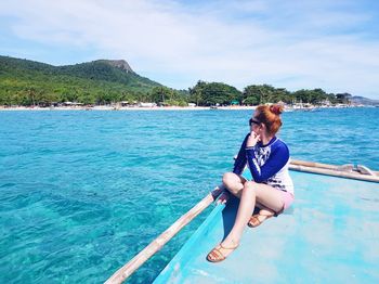 Woman sitting in sea against sky