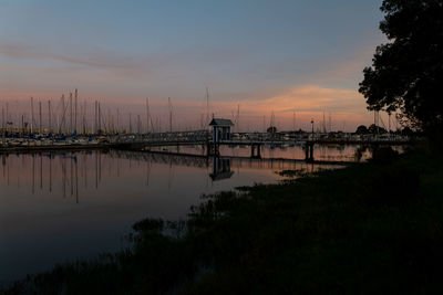 Sun setting behind pedestrian bridge leading to boats in harbor