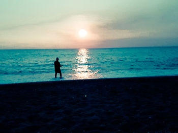 Silhouette people on beach against sky during sunset