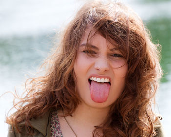 Portrait of young woman sticking out tongue against sky
