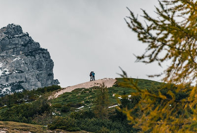 A couple of hikers standing on top of hill in mountains.