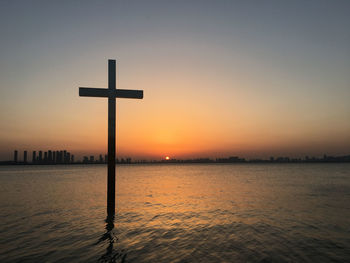 Silhouette of wooden post in sea during sunset