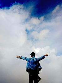 Rear view of man standing with arms outstretched against sky