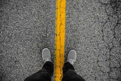 Low section view of person standing on yellow line of road