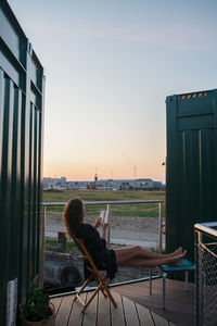 Rear view of woman sitting on chair at sunset
