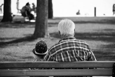 Rear view of girl with grandfather sitting on bench at park