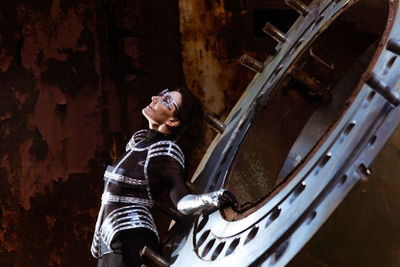 Strong woman in silver glasses and futuristic dress stands against the smoke in destroyed factory