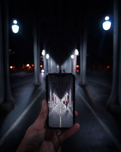 Midsection of person holding smart phone on street at night