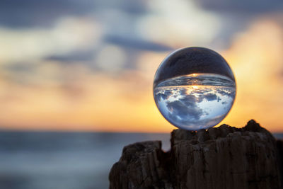 Close-up of crystal ball on rock against sea at sunset