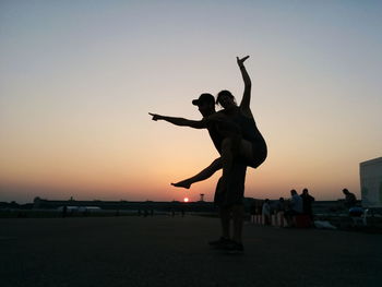 Silhouette man piggybacking woman at beach against clear sky during sunset