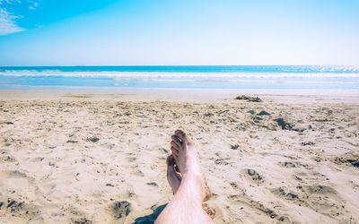 Low section of man relaxing at beach on sunny day