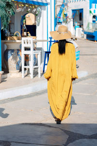 Beautiful african american woman in yellow dress and sun hat walks through streets