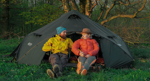 Man and woman sitting against tent on sunny day