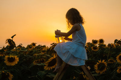 Woman standing on sunflower field against sky during sunset