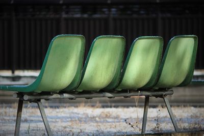 Close-up of empty green chairs in row on land