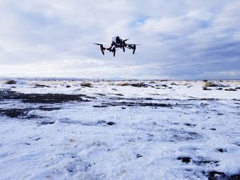 Drone flying over snow covered land against sky