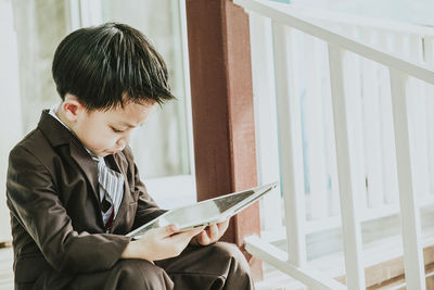 Boy in suit using digital tablet while standing on steps