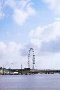 Ferris wheel by river against cloudy sky