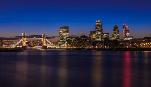 Illuminated buildings by river against sky at night