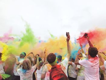 Group of people playing holi with colorful powder paints against clear sky