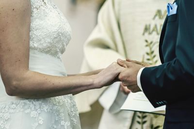 Midsection of groom holding bride by priest during wedding ceremony