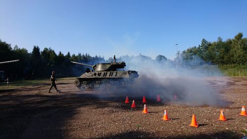 Armored tank emitting smoke on field against clear blue sky