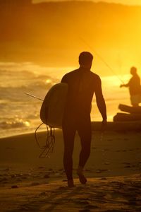 Silhouette man with surfboard walking at beach during sunset