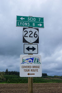 Sign board on field against cloudy sky