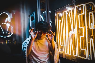 Rear view of man standing by illuminated lights at night