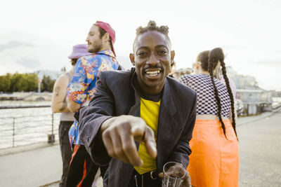 Portrait of smiling non-binary person dancing with friends in background on promenade