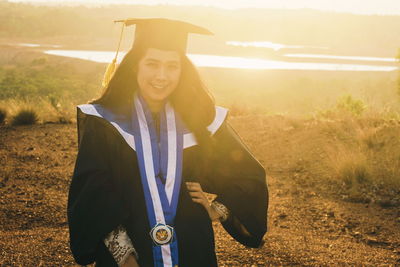 Portrait of young woman in graduation gown standing on field