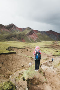 A young woman with a backpack is standing on a hill in peru