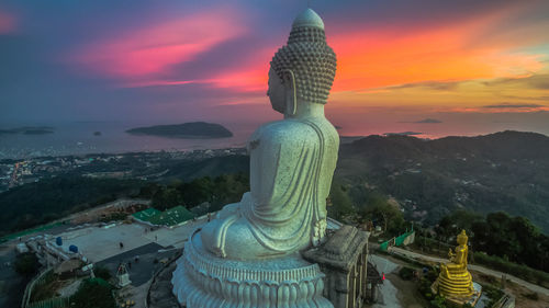 Giant buddha statue against sky at sunset