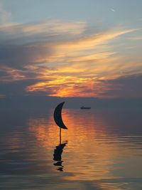 Silhouette bird on lake against sky during sunset