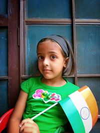 Portrait of girl holding indian flag while sitting against window