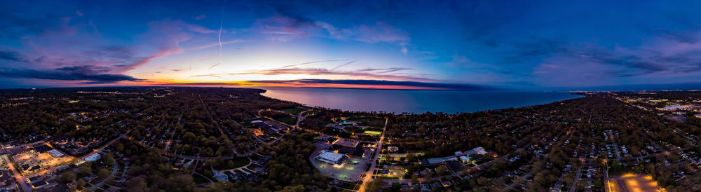 Illuminated city by sea against sky at sunset