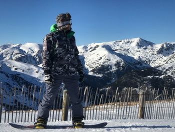 Full length of mid adult man snowboarding on field against clear blue sky