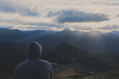 Rear view of man looking at mountains against cloudy sky