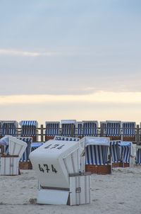 Hooded chairs on beach against sky during sunset