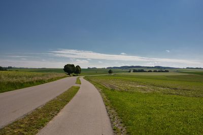 Empty road amidst field against sky