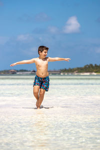 Full length of shirtless man jumping at beach