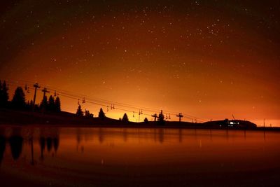 Silhouette bridge over river against sky at night