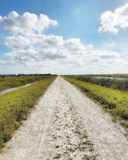 Dirt road amidst field against sky