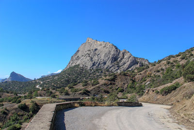 Road by mountain against clear blue sky