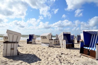 Hooded beach chairs on sand against sky