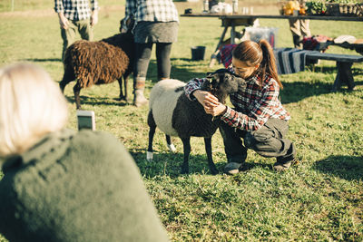 Mature female farmer embracing and kissing sheep on field