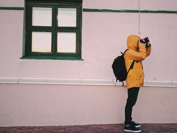 Side view of man photographing with camera while standing against building