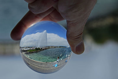 Close-up of hand holding crystal ball against sea